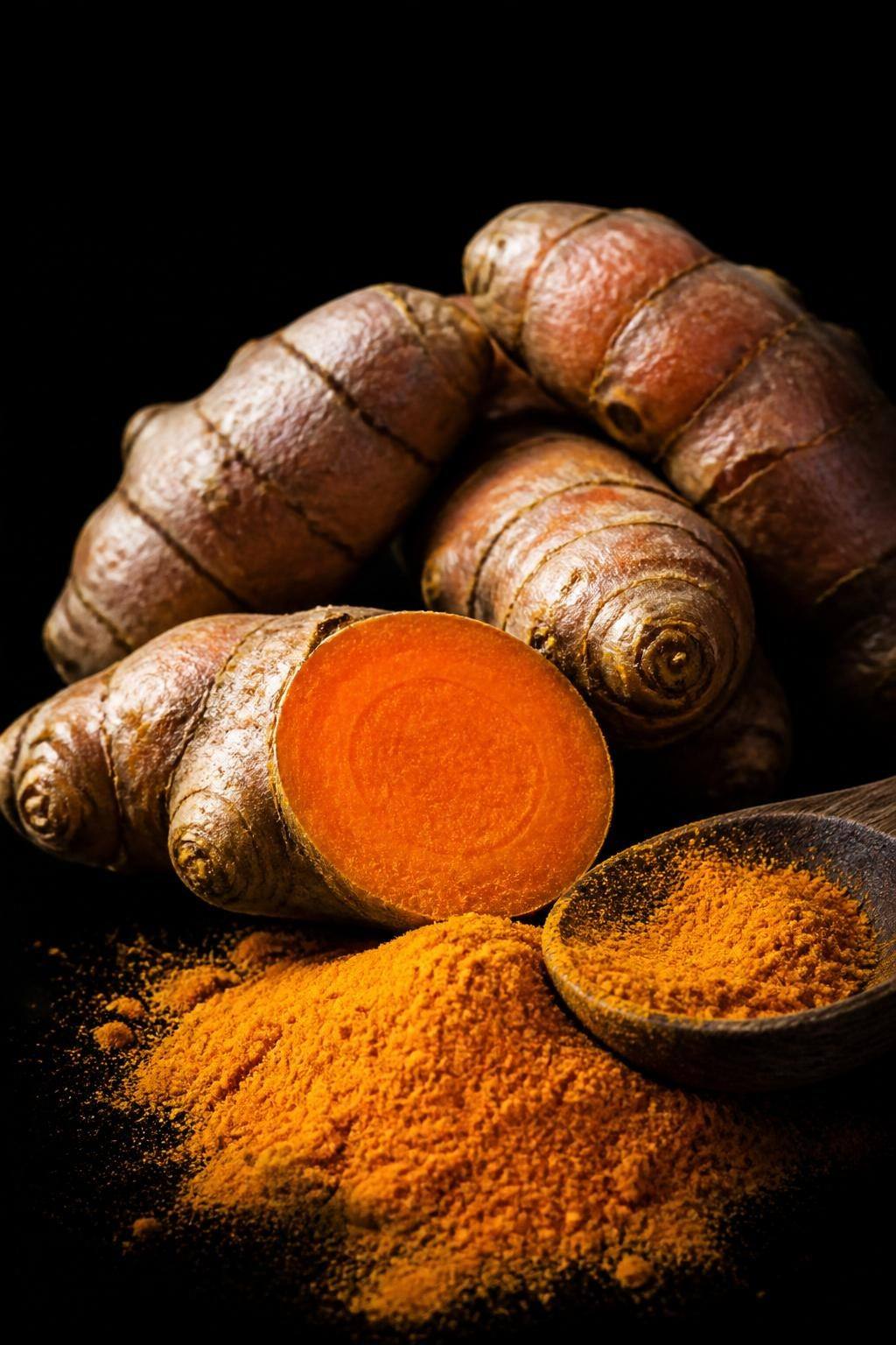 Macro botanique sur fond noir absolu — rhizomes de curcuma tranchés, chair orange incandescente, lumière directionnelle d'apothicaire.