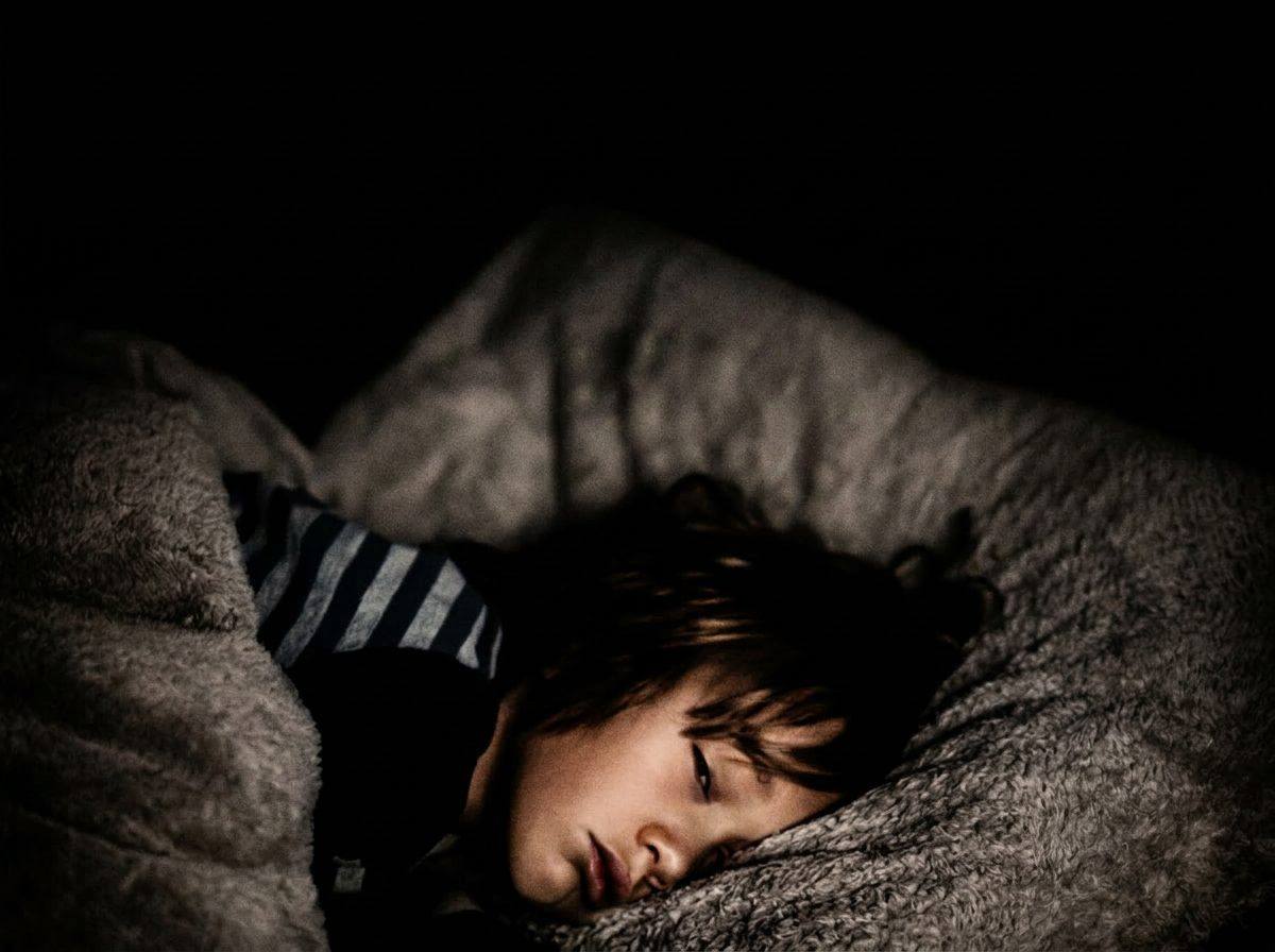 Portrait noir et blanc chiaroscuro — enfant endormi paisiblement dans la pénombre, lumière douce sur le visage.